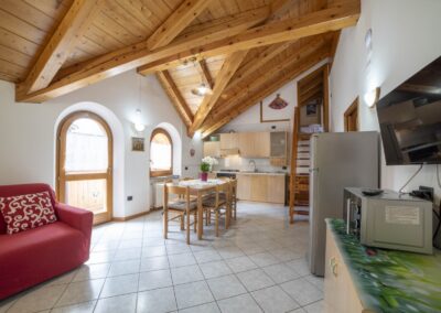 Zona giorno del Vioz con divano rosso, cucina e finestre ad arco