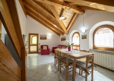 Soggiorno del Vioz con tavolo da pranzo, divano rosso e finestre ad arco