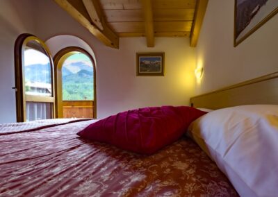 Letto matrimoniale del Vioz con copriletto rosso e finestre ad arco