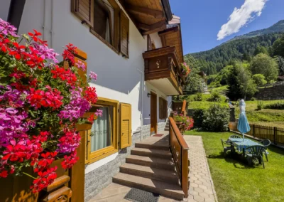 Facciata di Casa Bamby con gerani rossi, scala d'ingresso e giardino