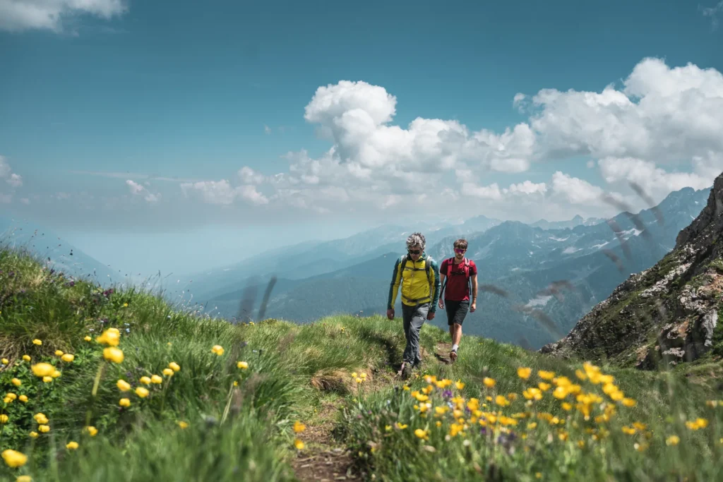 Due escursionisti su un sentiero fiorito in primavera, con le cime sullo sfondo